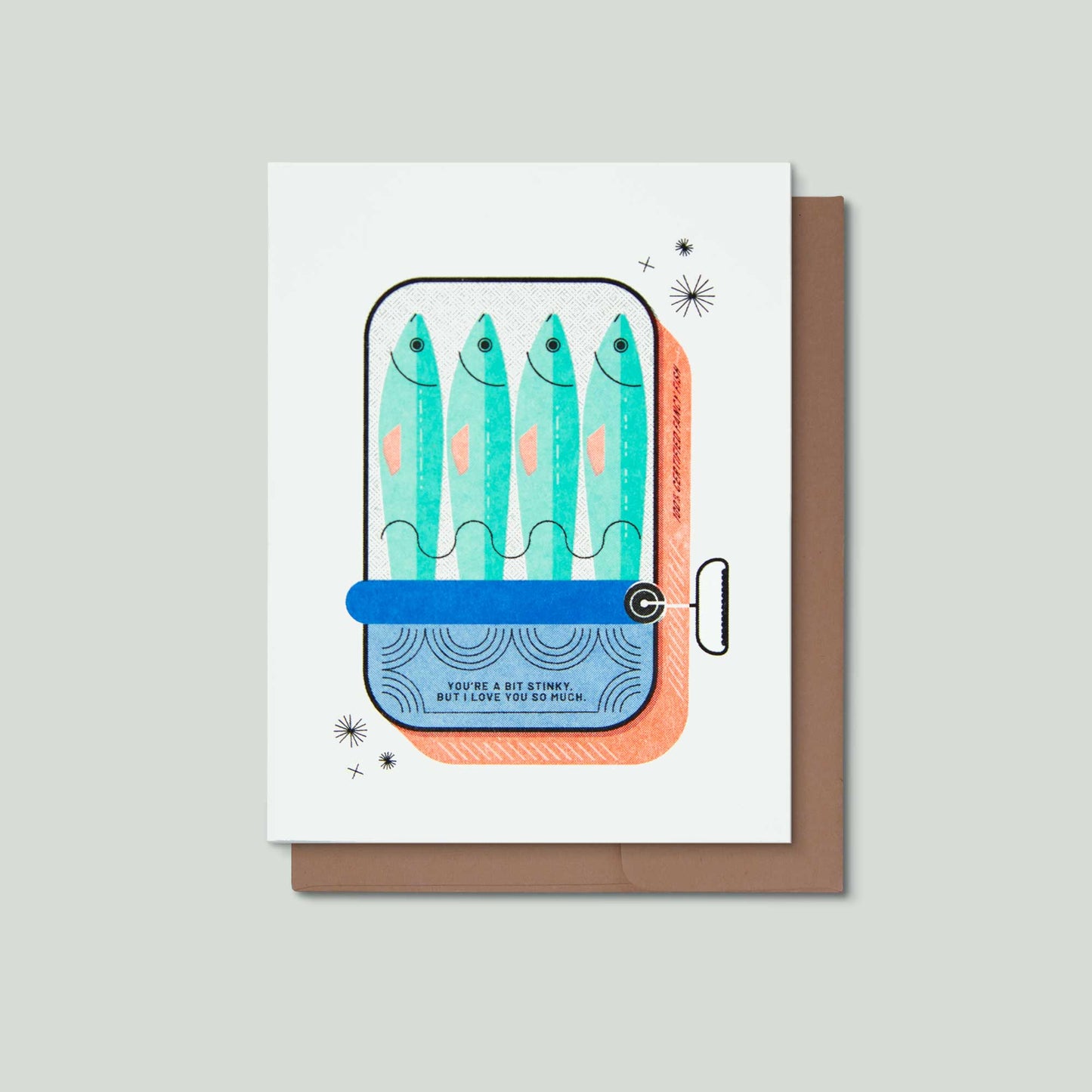 A greeting card with a whimsical illustration of four fish inside a can, shown with a brown envelope on a light gray background. The card features the text 'YOU"RE A BIT STINKY, BUT I LOVE YOU SO MUCH."