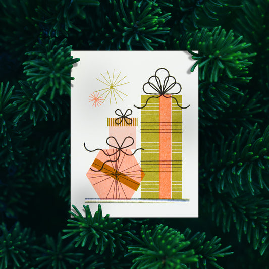 A greeting card featuring a minimalist illustration of three stacked gift boxes, set against a background of dark green pine needles.