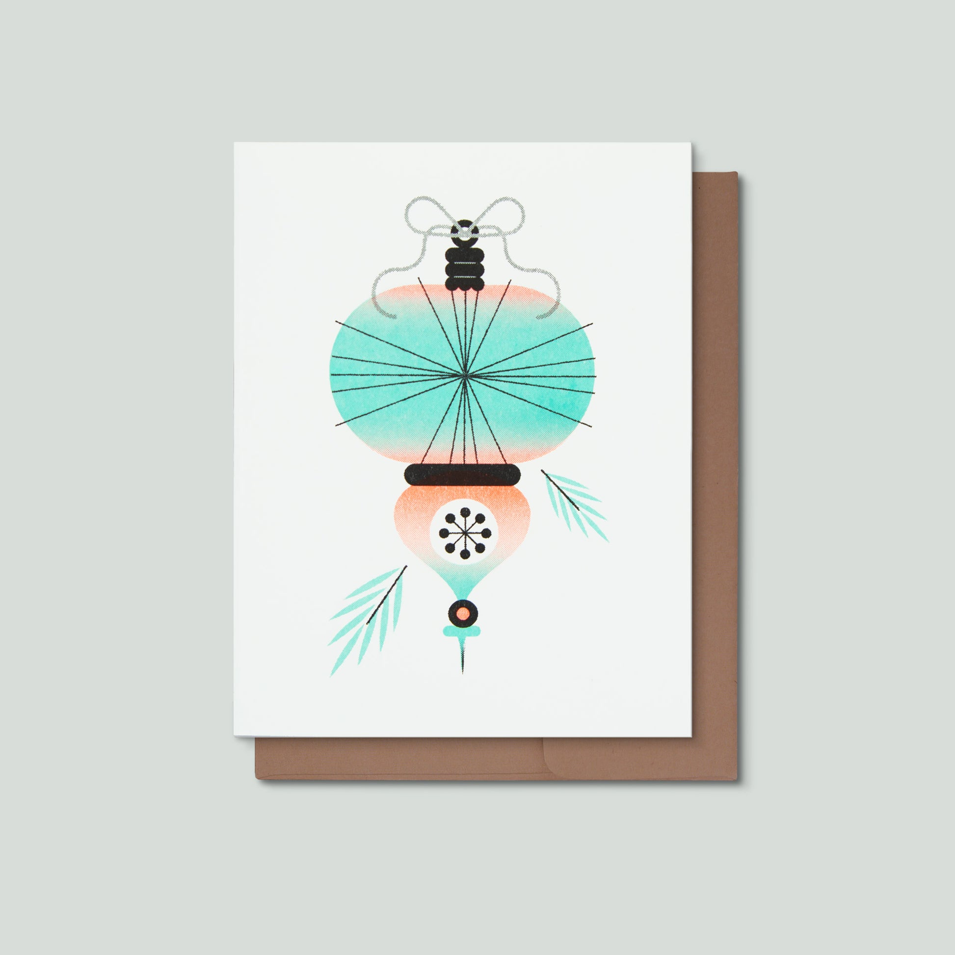 A greeting card featuring an illustrated Christmas ornament in front of a brown envelope and a grey background.