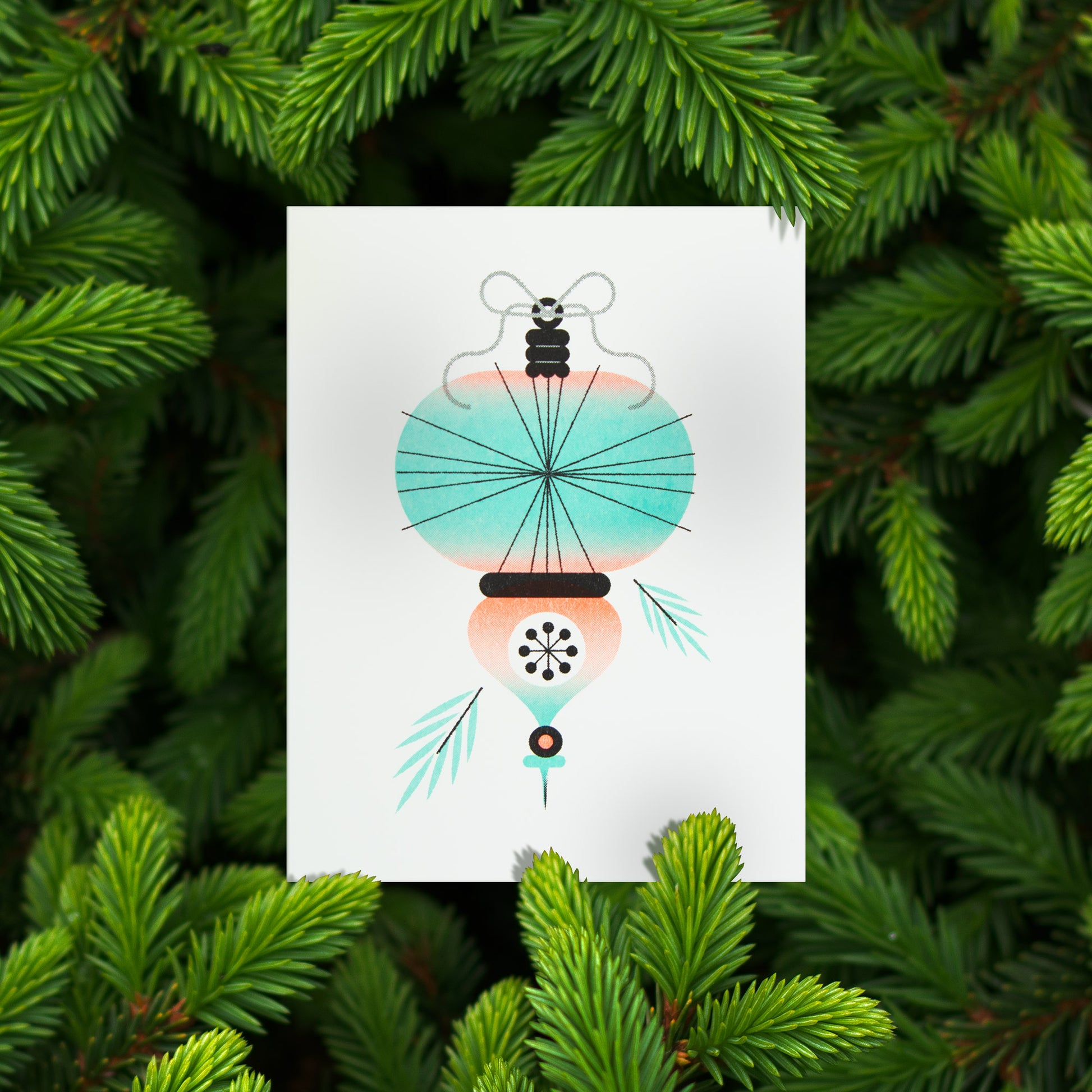 A greeting card featuring a stylized Christmas ornament, displayed against a background of green pine needles.