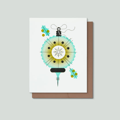 A white greeting card with a minimalist illustration of a christmas ornament, shown with a brown envelope on a light gray background.