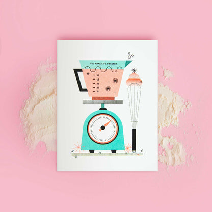 An illustrated risograph greeting card featuring a kitchen scale, measuring cup, and whisk displayed on a pink background with flour scattered over it.
