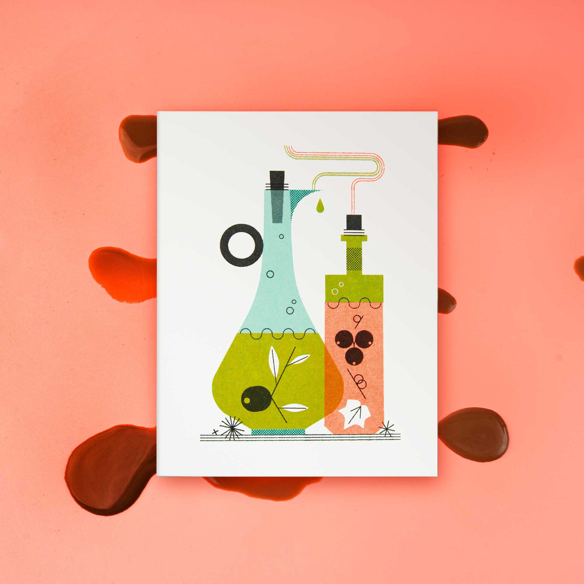 An illustrated risograph greeting card featuring a stylized illustration of oil and vinegar bottles, one light blue and one orange, with green and black details, displayed on a pink background with a splatter of balsamic vinegar.