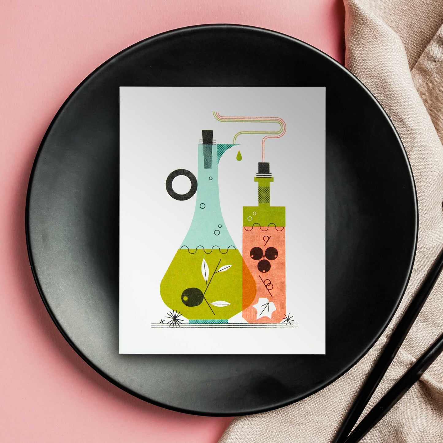 An illustrated risograph greeting card featuring a stylized illustration of oil and vinegar bottles, one light blue and one orange, with green and black details, displayed on a black plate over a pink background with a beige napkin and black utensils.