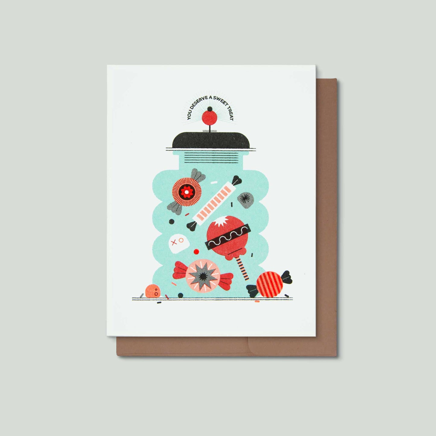 A white greeting card with a whimsical candy-themed illustration in red, black, and mint green, shown with a brown envelope on a light gray background.
