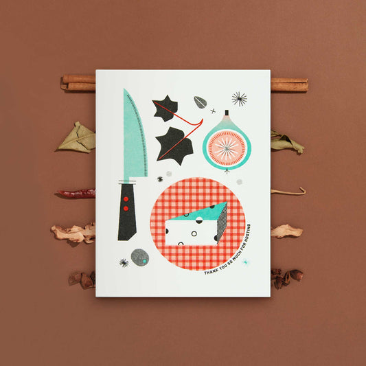 An illustrated risograph greeting card featuring illustrations of kitchen items and food, displayed on a brown background with dried herbs and peppers