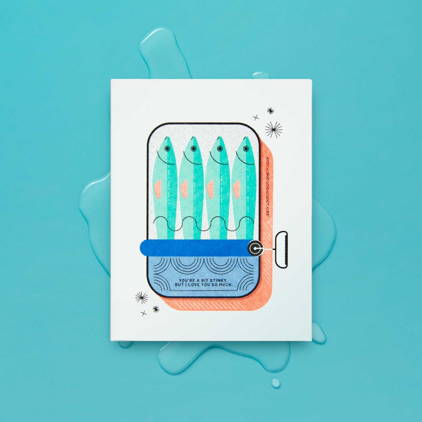 A white greeting card featuring a stylized illustration of four blue-green fish in a sardine tin, with the text 'YOU'RE A BIT STINKY BUT I LOVE YOU SO MUCH', placed on a turquoise background with liquid splash graphics.
