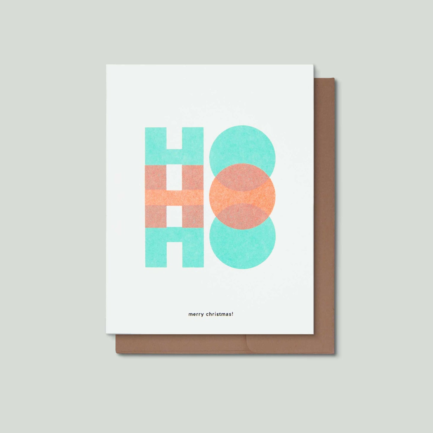 A risograph greeting card with colorful lettering that says Ho Ho Ho merry christmas! in front of a brown envelope on a light grey background.
