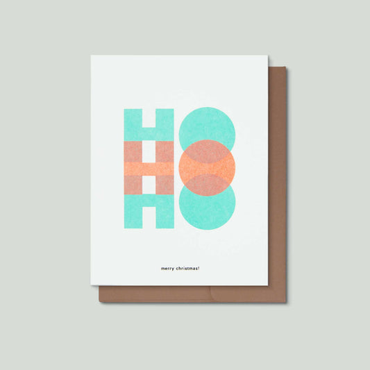 A risograph greeting card with colorful lettering that says Ho Ho Ho merry christmas! in front of a brown envelope on a light grey background.