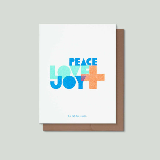 An illustrated typographic risograph greeting card that says Peace, Love + Joy in the middle in large bold colorul  font, and this holiday season small at the bottom. It is front of a kraft brown envelope on a grey background.