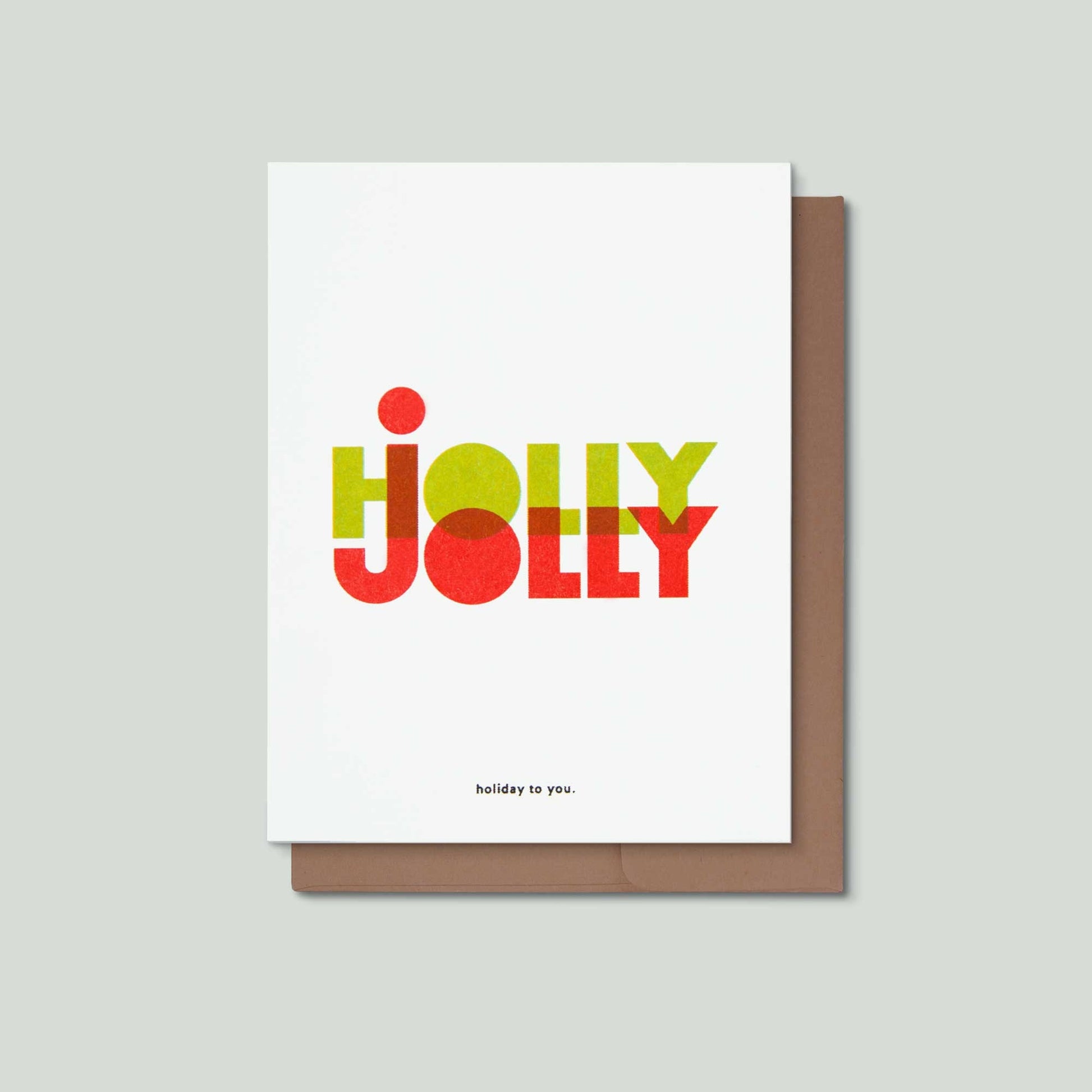 A white greeting card with the word 'HOLLY JOLLY' in large colorful letters in the middle, and 'holiday to you.' at the bottom, shown with a brown envelope behind it on a light gray background.