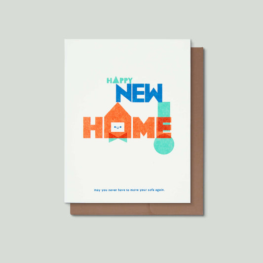 A risograph greeting card with whimsical typography that says happy new home! may you never have to move your sofa again. The "o" in the word home is replaced with a smiling house shape. The card is in front of a brown envelope on a light grey background.