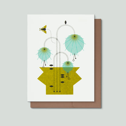 Photo of a risograph greeting card with an illustration of blue flowers in a green vase with a small flying moth on a light grey background.