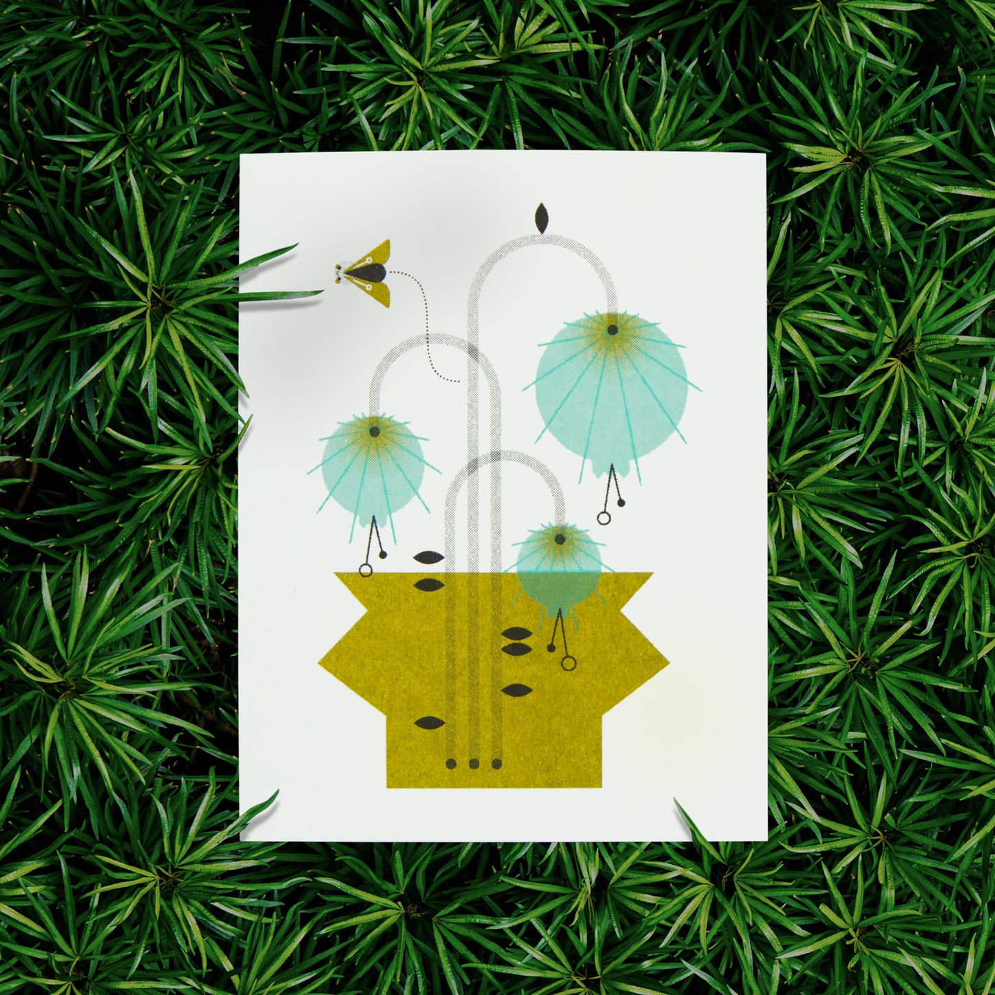 Photo of a risograph greeting card with an illustration of blue flowers in a green vase with a small flying moth on a green plant background.