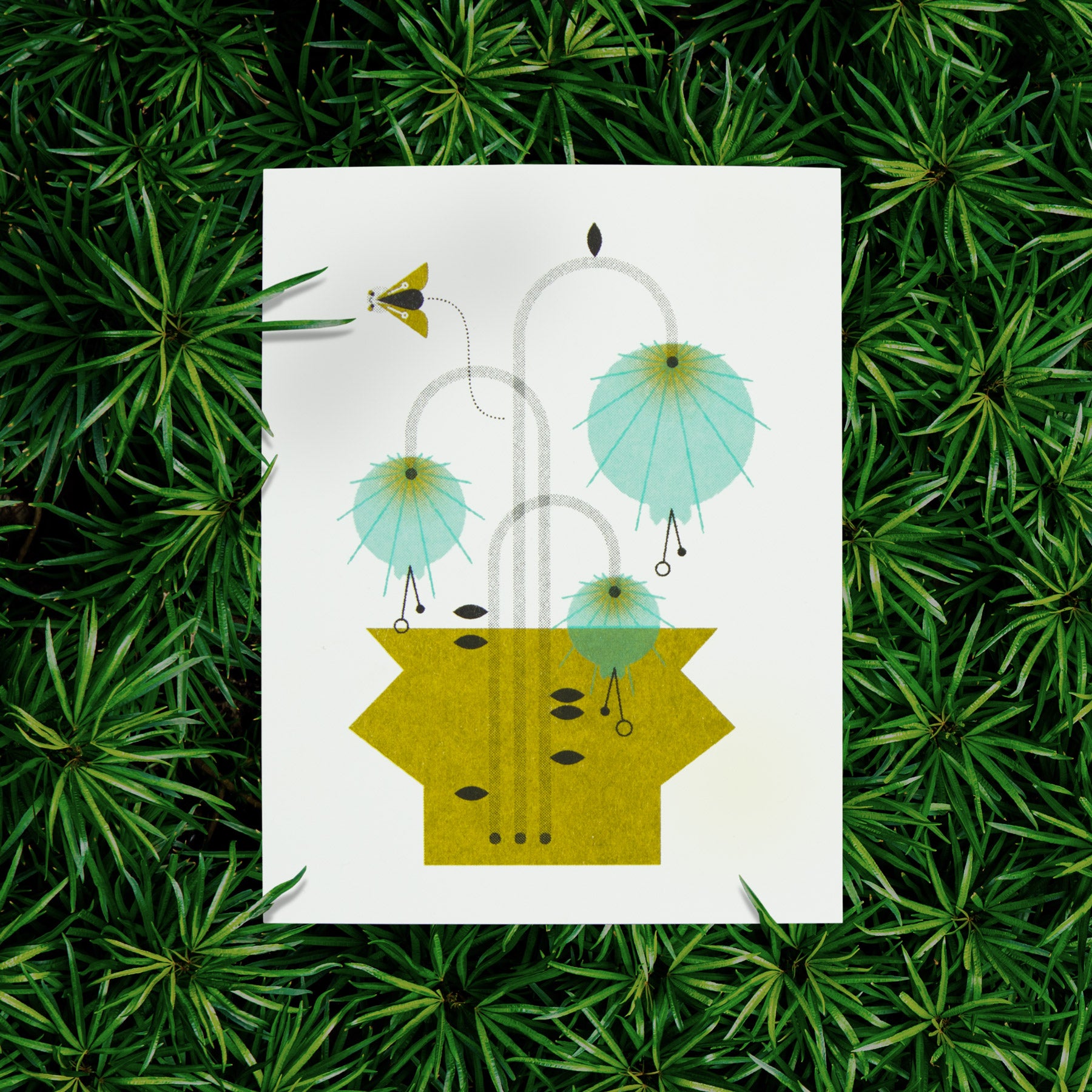 Photo of a risograph greeting card with an illustration of blue flowers in a green vase with a small flying moth on a green plant background.