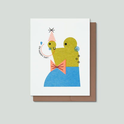 Greeting card with a colorful illustration of a frog and text that says Oh Hoppy Day on a white background