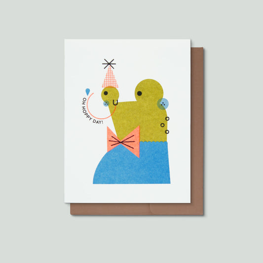Greeting card with a colorful illustration of a frog and text that says Oh Hoppy Day on a white background