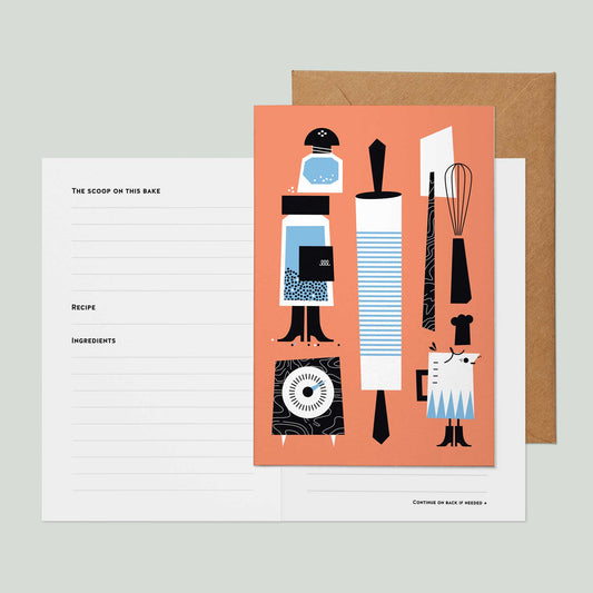 A recipe card greeting card featuring a salmon pink front cover illustrated with kitchen utensils and tools in black, white, and light blue, shown with a brown kraft envelope and a white lined recipe insert page on a light gray background.
